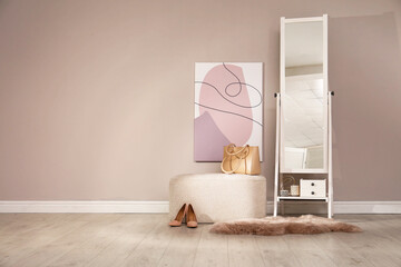 Poster - Stylish pouf and mirror near beige wall indoors. Space for text