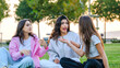 © HI Pictures - Three young female friends chatting and having fun together in a grassy park on a summer day.