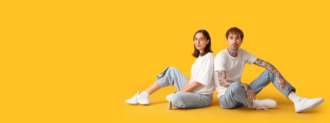 Wall Mural - Young couple in stylish jeans on yellow background with space for text