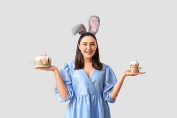 Canvas Print - Happy young woman in bunny ears with sweet Easter cakes on grey background