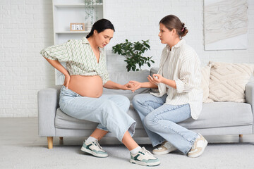 Wall Mural - Young doula holding pregnant woman's hand on sofa at home