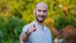 © HI Pictures - A middle-aged handsome businessman pointing his index finger toward the camera to show approval in a tree-lined park on a summer day