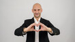 © HI Pictures - In a studio setting, a middle-aged businessman wearing a suit is standing in front of a white background, making a heart shape with his hands and looking at the camera