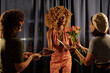 © pressmaster - Woman smiling while holding flowers, surrounded by two friends during special event. Joy and laughter radiating from group celebrating occasion and sharing joy
