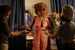 © pressmaster - Smiling African American woman holding flowers while celebrating with friends in cozy home setting filled with warm lighting and cheerful atmosphere