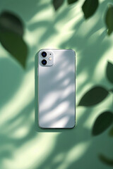 Poster - modern smartphone resting on a green surface with soft shadows and leaves creating an aesthetic arra