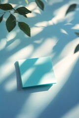 Poster - bright turquoise notepad resting on a light surface with delicate leaves casting playful shadows dur