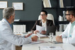 © pressmaster - Portrait of mature woman as female boss talking to doctors while sitting at table during management meeting in clinic