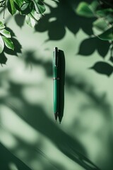 Poster - Green pen resting on a muted surface surrounded by soft shadows of leaves creating an inviting workspace atmosphere