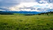 © Generative AI - Vast green field under a dramatic sky filled with clouds and distant mountain ranges : Generative AI