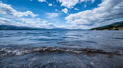 Aufkleber - Serene lakeside view with gentle waves reflecting a cloudy sky and distant mountains : Generative AI