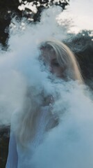 Aufkleber - A figure enveloped in soft, swirling clouds of blue mist stands amidst nature at dusk, creating an enchanting and mysterious atmosphere as daylight fades