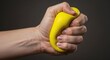 © Rifqi - Close-up of a hand squeezing a bright yellow stress ball against a dark gray background, concept for stress relief, therapy, and anxiety management