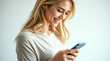 © Nastassia - A young girl looks at the smartphone screen with a smile. She is dressed in a light blouse, and her long hair falls beautifully on her shoulders. The background is minimalistic.