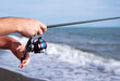© isavira - Spinning fishing. Close-up of male fisherman hands catching fish with spinning rod at sea on sunny hot day against blue sky background