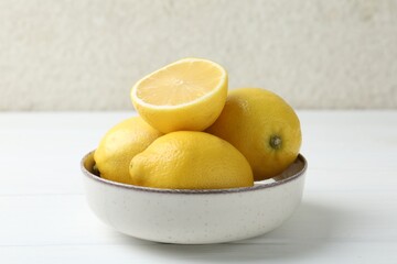 Wall Mural - Fresh whole and cut lemons in bowl on white wooden table, closeup