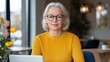 © Elena - Middle-aged woman wearing glasses in a bright sweater working on a laptop in a cozy cafe setting