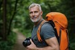 © Andrii Zastrozhnov - A man with a beard and gray hair is wearing an orange backpack and holding a camera. He is a photographer, possibly taking a photo of the forest