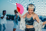 Young woman dancing with hand fan and headphones at summer music festival