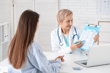 Wall Mural - Happy mature female doctor showing test results to patient in clinic