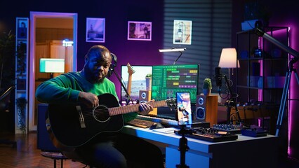 Poster - Professional composer teaching guitar lessons online on master class, recording himself playing acoustic instrument accords and explaining notes for tutorial. Young musician making vlogs. Camera B.