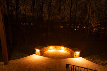 Wall Mural - a backyard patio covered in fresh snow with a curved stone wall glowing under warm lights at night. 