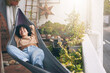 © peopleimages.com - Happy woman, relax or lying with hammock on balcony in garden for morning or fresh air at home. Female person, comfort or hanging bed with plants on terrace for rest, break or calming zen at house