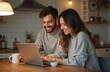 © miss irine - Cheerful couple looks at laptop screen sitting at kitchen table. Smiling spouse web surfing, making purchases online or booking flight tickets. Couple wearing casual clothes using notebook indoor.