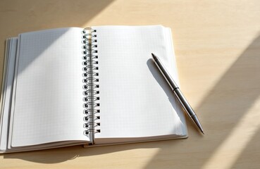 Poster - Open notepad with blank pages with grid, lying on wood table in sun light. Pen rests beside journal. Copy space, template. Education, business and self-development concept.