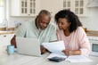 © KumCup - Focused Couple Reviewing Finances at Home with Laptop and Paperwork in a Cozy Kitchen Setting
