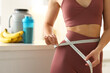 © New Africa - Weight loss. Woman measuring waist with tape in kitchen, closeup