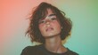 © Bundi - With short hair and dressed in casual orange, a confident nonbinary person poses against a vibrant pink and teal background in a studio portrait, embodying modern style and inclusivity