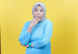 © Iqy - An asian woman in a hijab and blue shirt covers her mouth in surprise, expressing shock or disbelief.