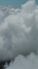 Wall Mural - flying through beautiful white fluffy clouds in sky over blue sea. airplane travel background. verti