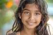 © imagemir - A smiling young girl with long, wavy hair and expressive brown eyes, exuding warmth and joy in a vibrant outdoor setting.