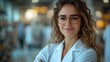 © MST - A smiling female pharmacist with long, wavy hair and glasses stands confidently with her arms crossed in a pharmacy.
