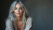 © MST - A middle-aged woman with long, silver-gray hair poses thoughtfully against a textured, light-colored background.
