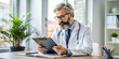 © Alisa - Concentrated doctor with beard and glasses is sitting at a desk and carefully reviewing patient information on a clipboard in his office