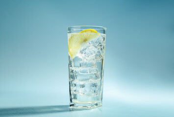 Wall Mural - Soda water with lemon and ice cubes in glass on light blue background