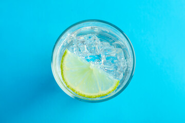 Wall Mural - Soda water with lime and ice cubes in glass on light blue background, top view