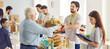 © Studio Romantic - Young cheerful man working at charity center with a team of volunteers and giving free food donations in charitable foundation for people in need. Humanitarian aid and volunteering concept. Banner.