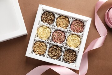 Wall Mural - Delicious flower shaped chocolate bonbons in box on brown background, flat lay