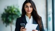 © warunthorn - Confident Businesswoman Holding Paper and Smartphone in Office Setting