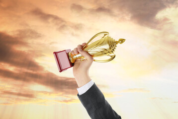 Wall Mural - man holding golden trophy against sunset sky, closeup