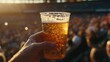 © RealityForge - A hand holding a beer in a plastic cup at a sports stadium during sunset with warm lighting.