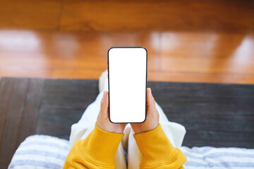 Wall Mural - top view mockup image of a woman holding mobile phone with blank desktop screen while sitting in bed
