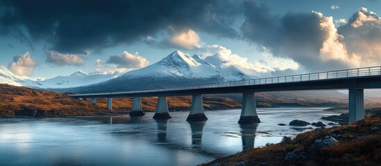 Aufkleber - Breathtaking landscape featuring Skye Bridge over tranquil water with snow-capped mountains in background, dramatic clouds above, and earthy tones below.