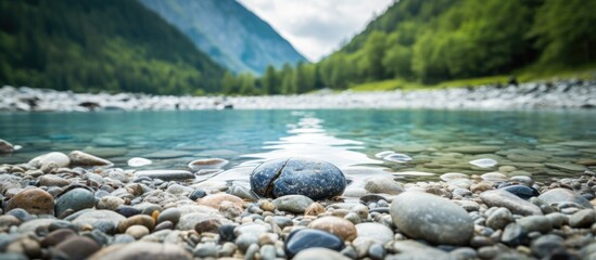 Aufkleber - Mountain river basin featuring a smooth stone at the center with a turquoise water surface, surrounded by pebbles and lush green hills in background.