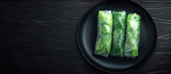 Poster - Fresh Spring Rolls on a black plate arranged on a dark textured wooden surface with a minimalist style showcasing vibrant greens