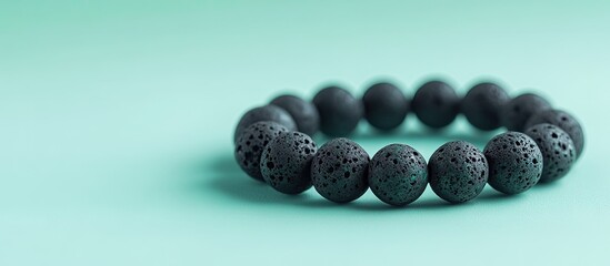 Poster - Black lava stone bracelet on a soft mint green background, featuring textured beads arranged in a circular pattern, showcasing elegance and simplicity.
